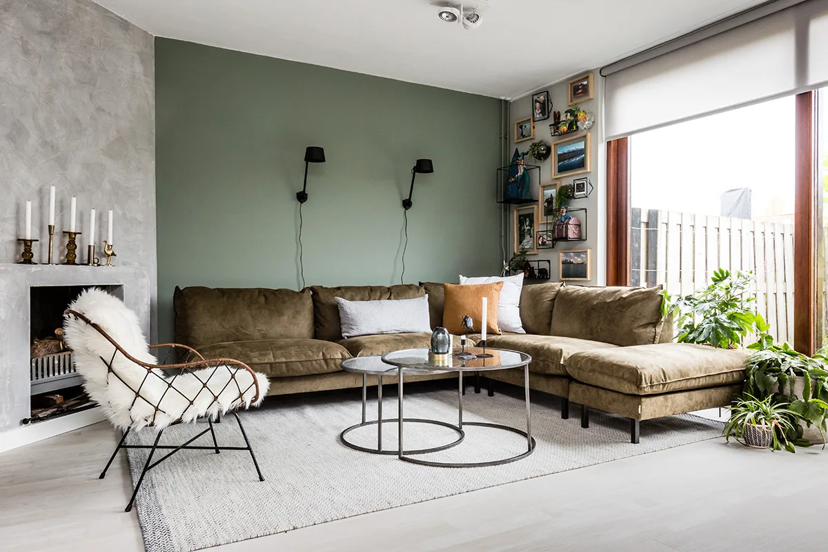 Woonkamer met groene wand, bank en natuurlijke materialen