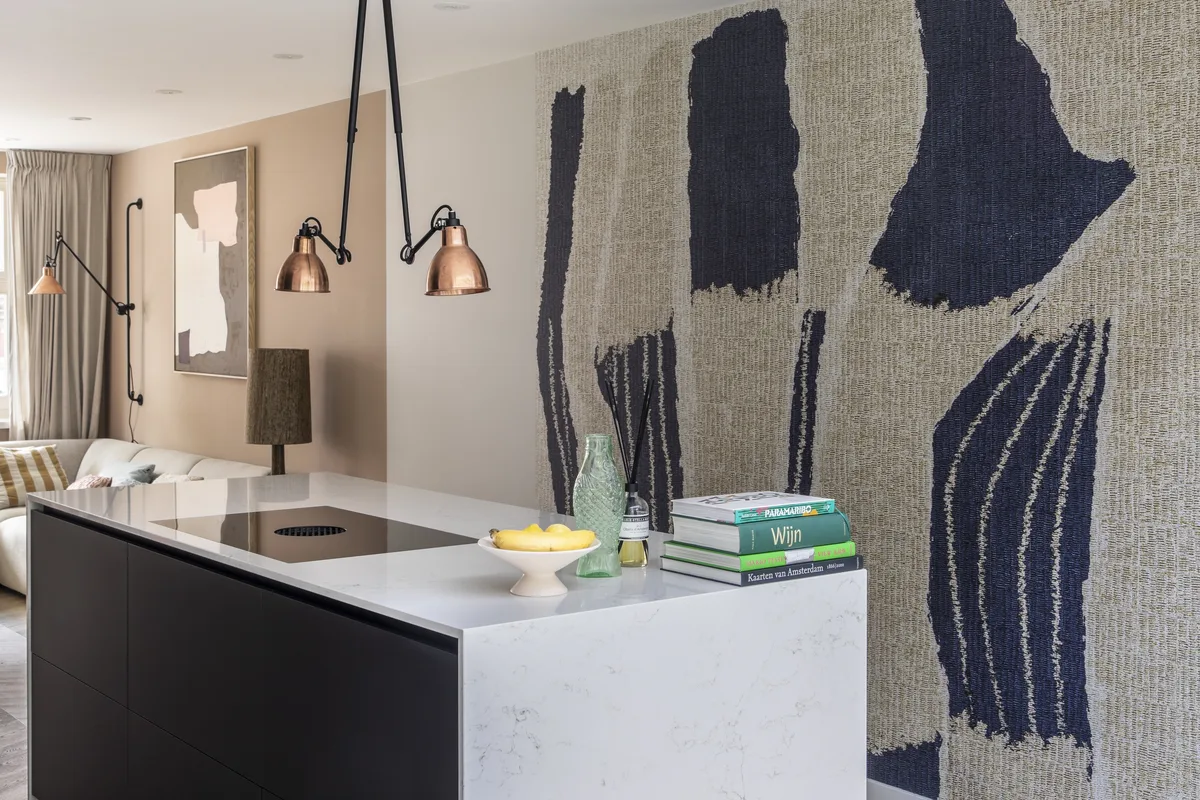 Afgeronde leefruimte met keukeneiland, koperen lampen en een wand met textielkunst